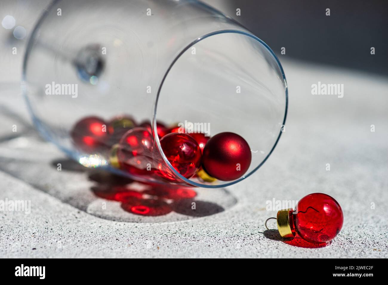 Primo piano di mini decorazioni natalizie che si riversano da un bicchiere come un bicchiere di vino rosso caduto Foto Stock