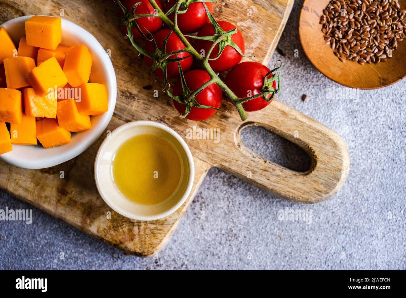 Vista dall'alto dei pomodori ciliegini, dei cubetti di formaggio, dell'olio d'oliva e dei semi di lino su un tagliere Foto Stock