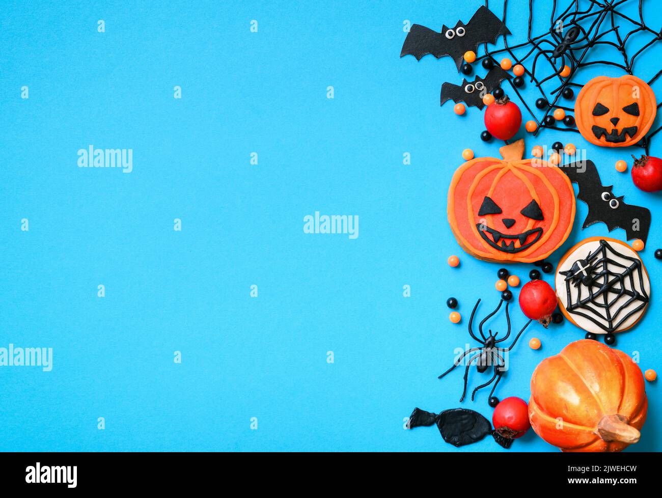 Dolci di Halloween e decorazioni su sfondo blu. Vista dall'alto di biscotti di Halloween, zucca d'arancia, ragni, ragnatela e pipistrelli, e spazio, giacitura piatta. Concep Foto Stock