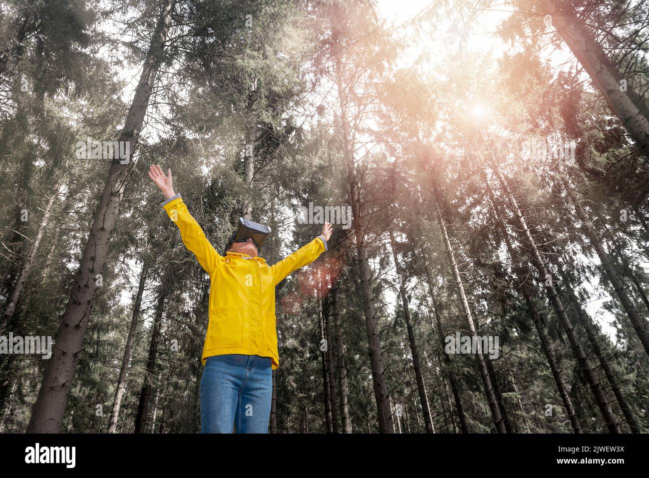 Donna che indossa cuffie per realtà virtuale in piedi in una foresta Foto Stock
