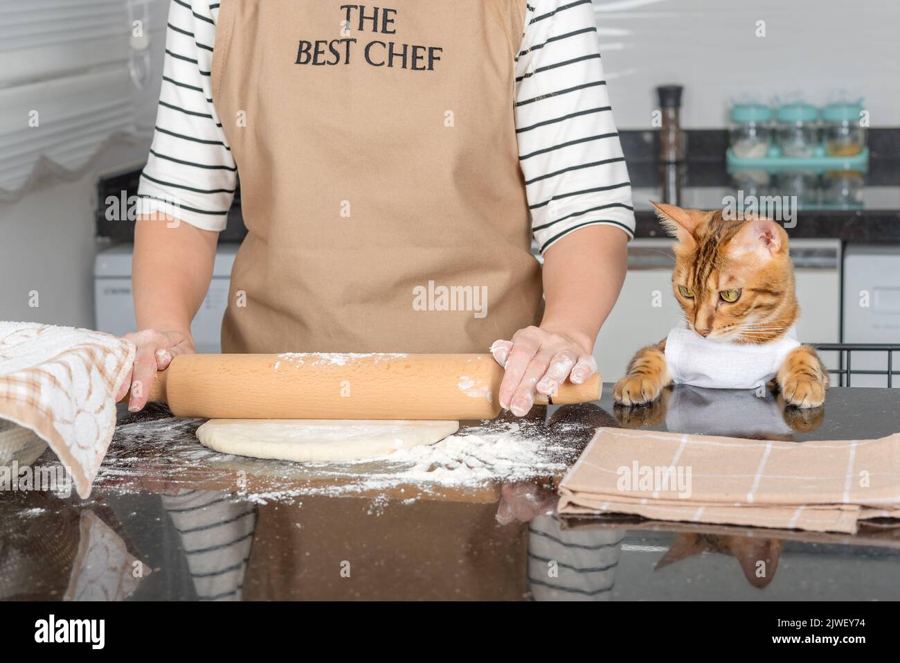 Una donna in grembiule, prima di preparare la pizza, stenderà l'impasto sul tavolo da cucina utilizzando un matterello. Foto Stock