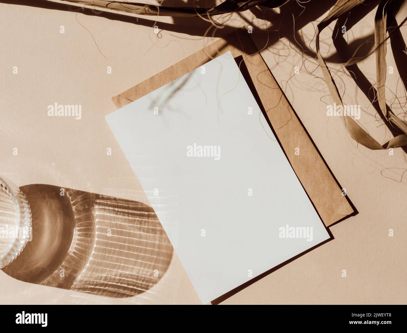 Cartoncino bianco vuoto, busta e parte di foglia di palmo secco su sfondo beige vista dall'alto. Elemento di design per l'invito di nozze, grazie biglietto, saluto, busin Foto Stock