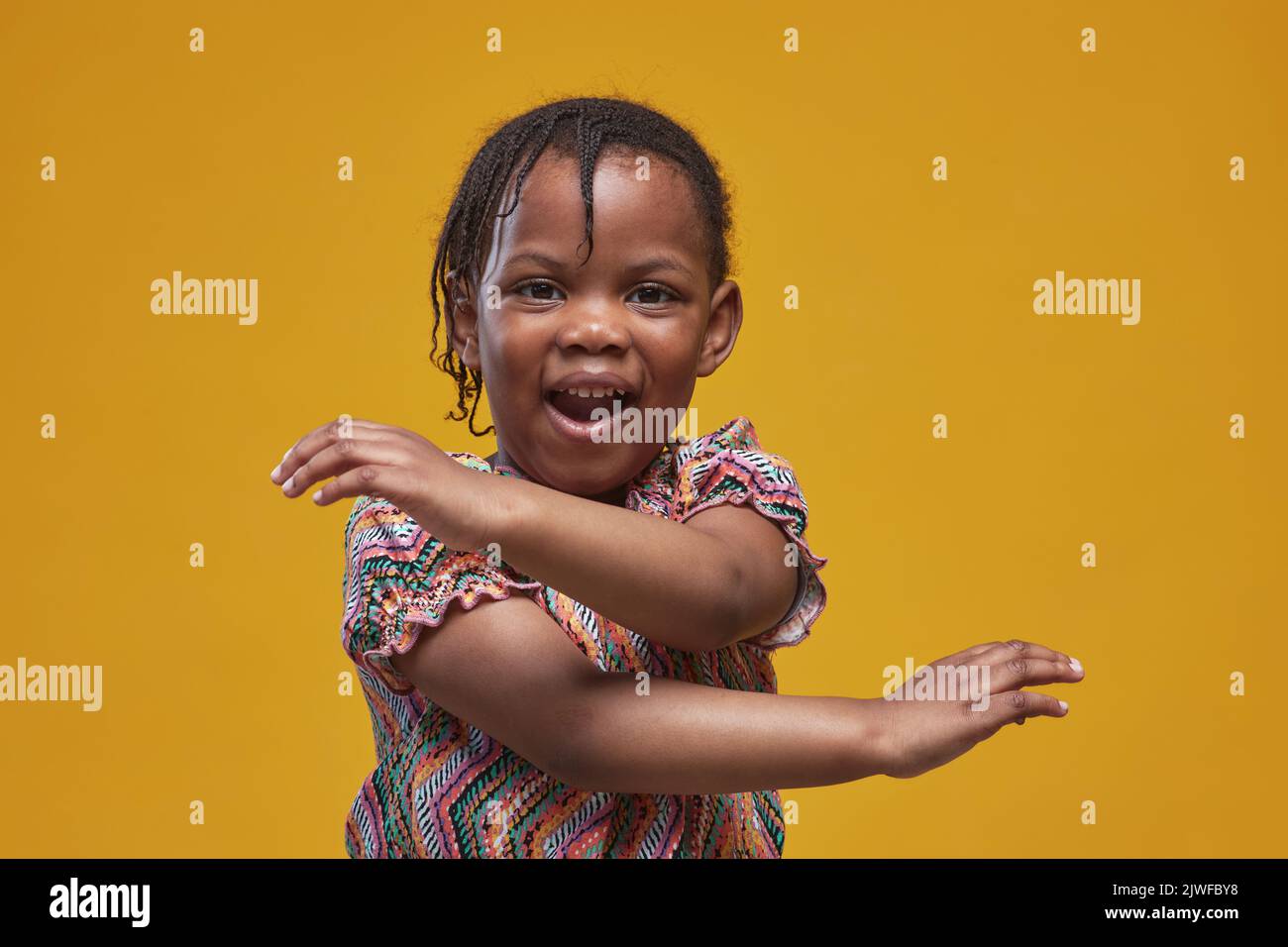 Ritratto di giocosa bambina africana che si folo intorno su sfondo giallo Foto Stock