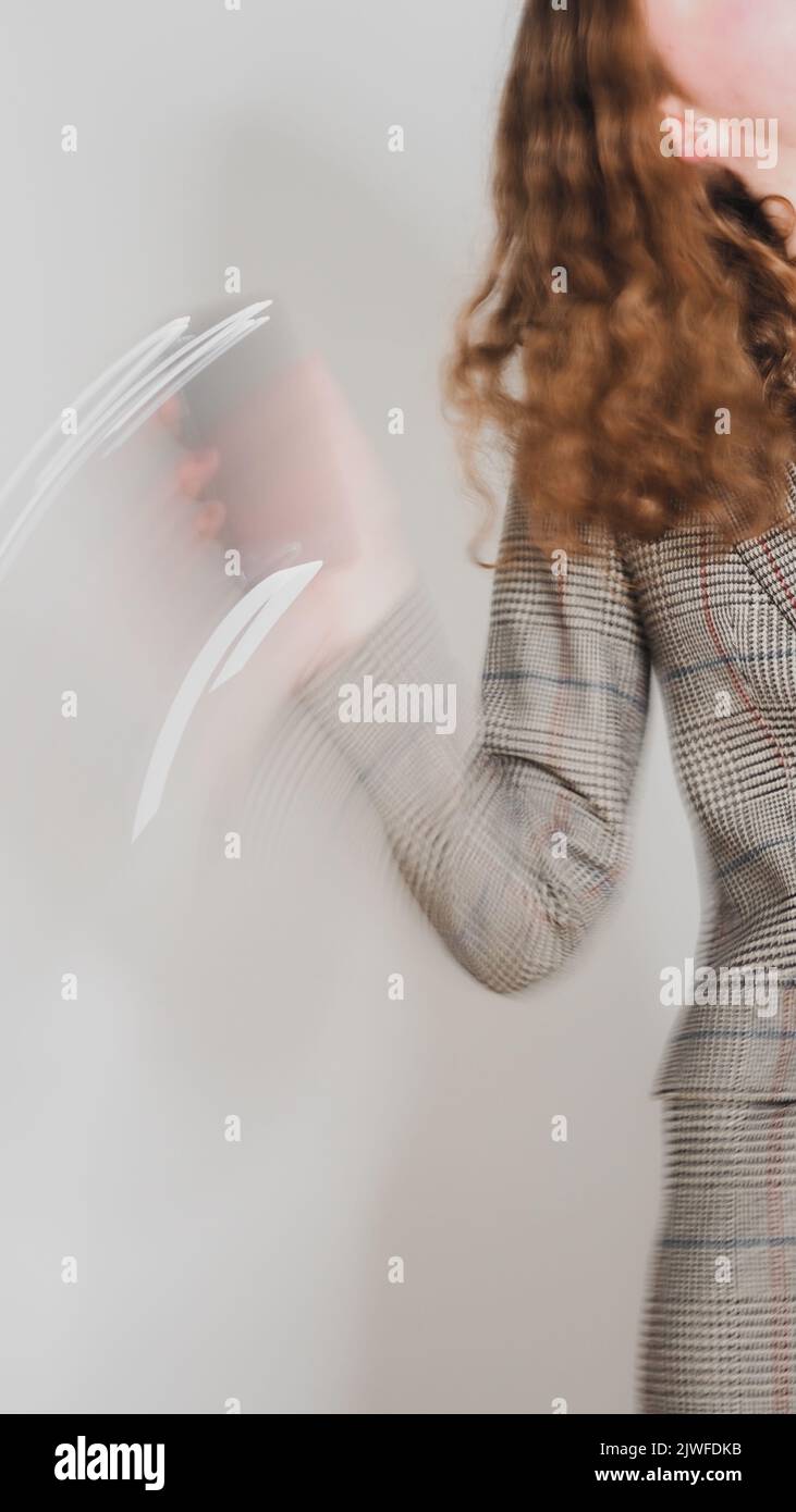 Una brunetta ricci femmina in una tuta che tiene un telefono cellulare in movimento sfocato Foto Stock