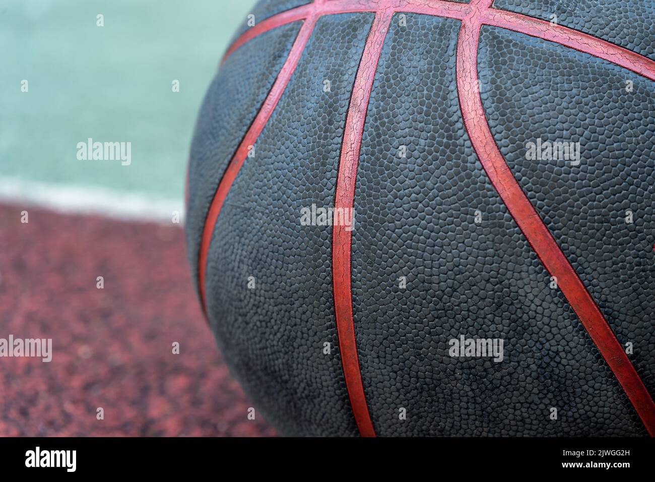 Palla da basket nera a terra. Primo piano sul campo rosso. Pallacanestro sulla strada o campo al coperto. Abbigliamento sportivo senza persone. Minimalismo. Foto Stock