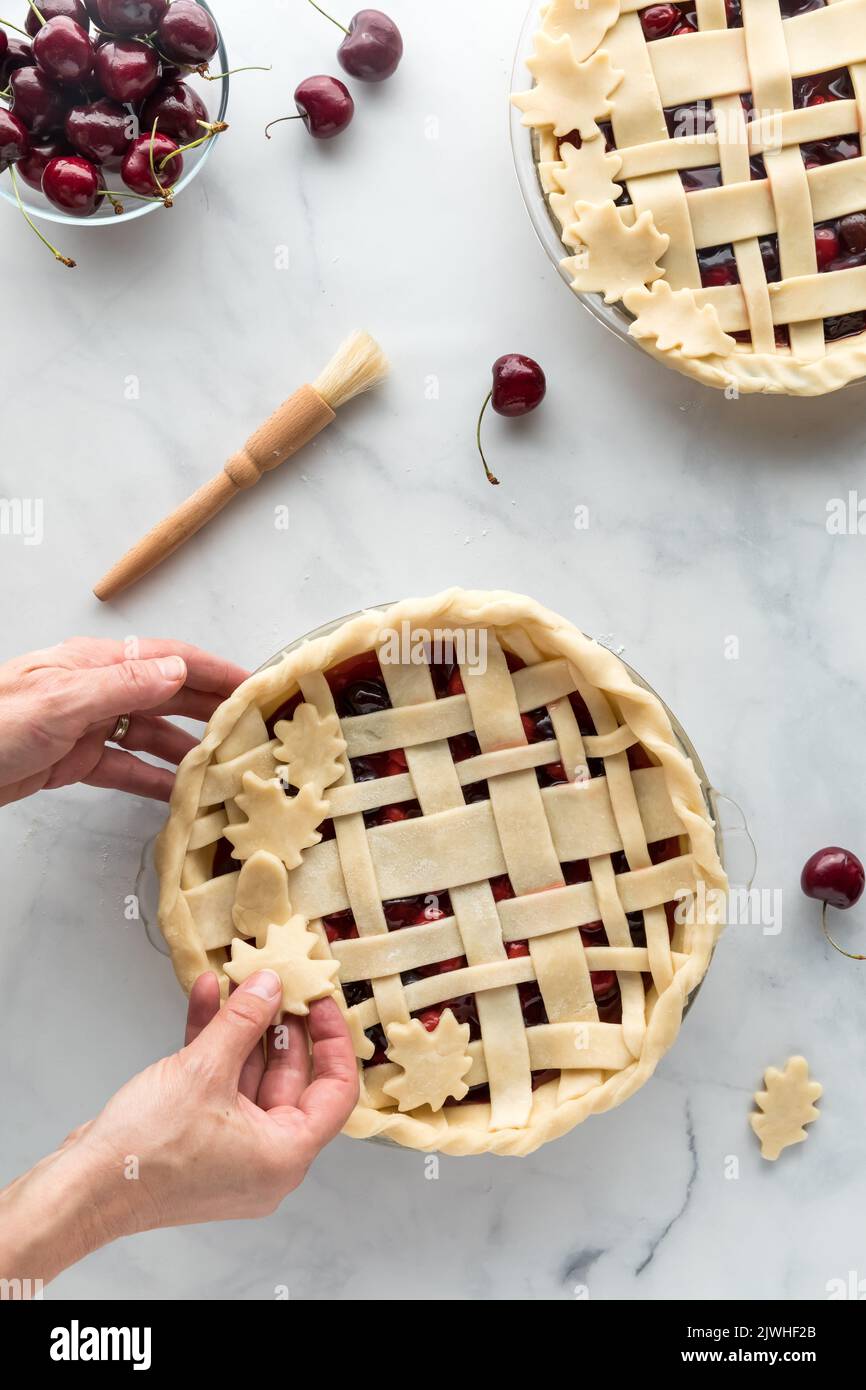 Preparare torte di ciliegia per la cottura con le mani mettendo su foglie decorative. Foto Stock