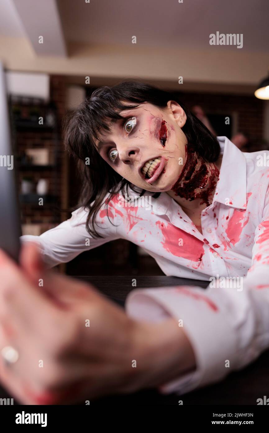 Donna diavolo zombie guardando il notebook, camminare cadavere sanguinoso morto cercando di lavorare in ufficio. Spaventoso camminatore pericoloso spaventoso con cicatrici e ferite, mangiare cervello ed essere posseduto. Foto Stock