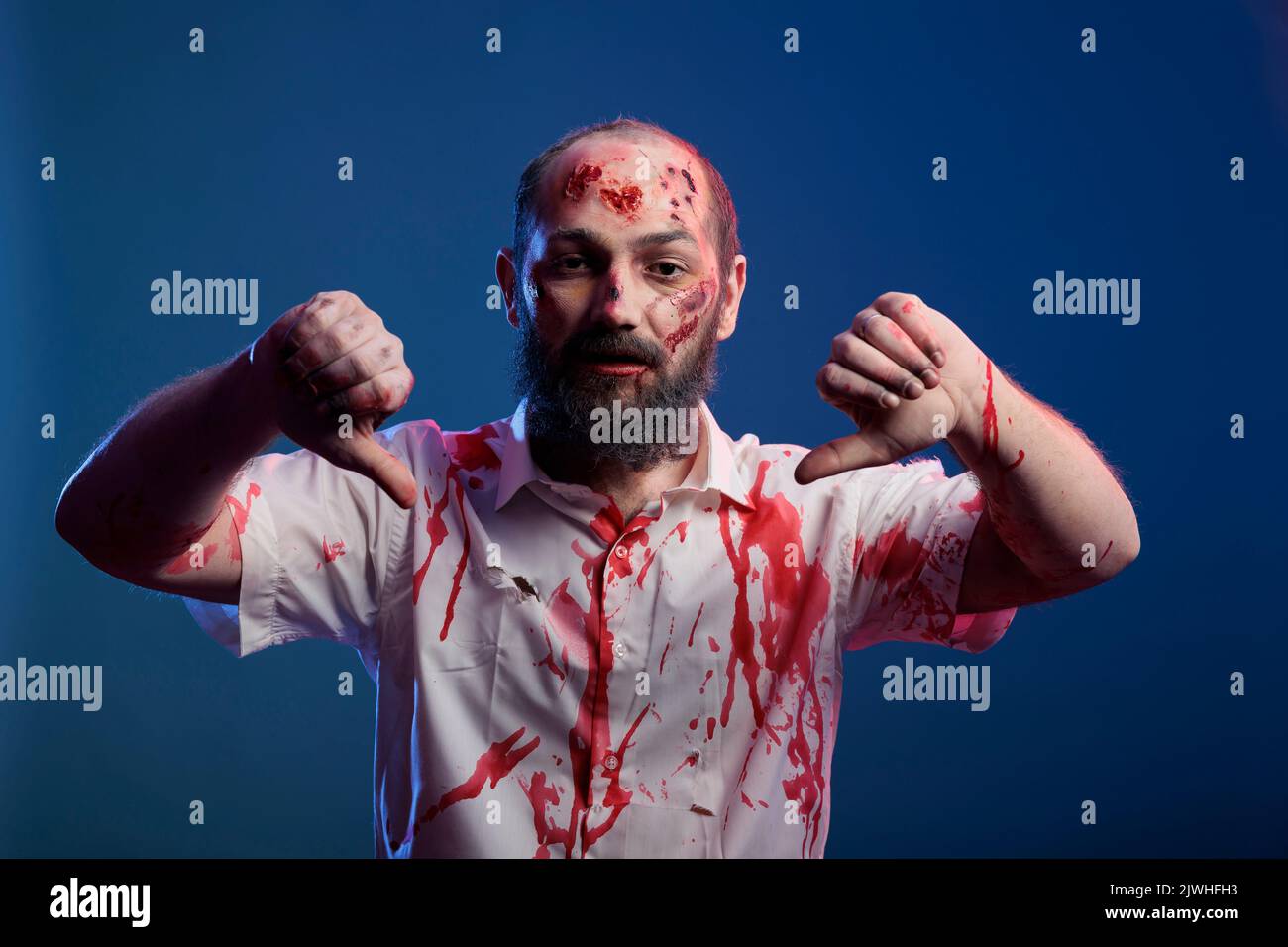 Zombie creepy fare i pollici giù gesto in studio, esprimere dispiacere e disapprovazione segno sulla fotocamera. Cadavere aggressivo e pericoloso con occhi malvagi mostro e ferite sanguinose, thriller horror. Foto Stock