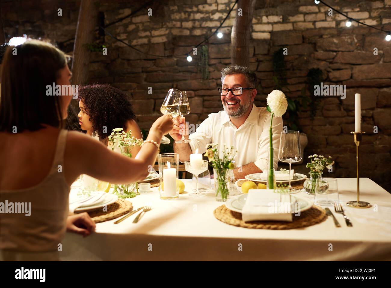 Allegro uomo maturo e giovane ospite clinking con wineglass sopra servito tavolo festivo mentre godendo festa di nozze Foto Stock