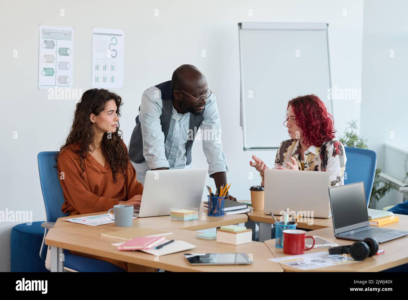 Due manager interculturali che ascoltano la loro collega che spiega la sua idea di un nuovo progetto di business durante la discussione alla riunione Foto Stock