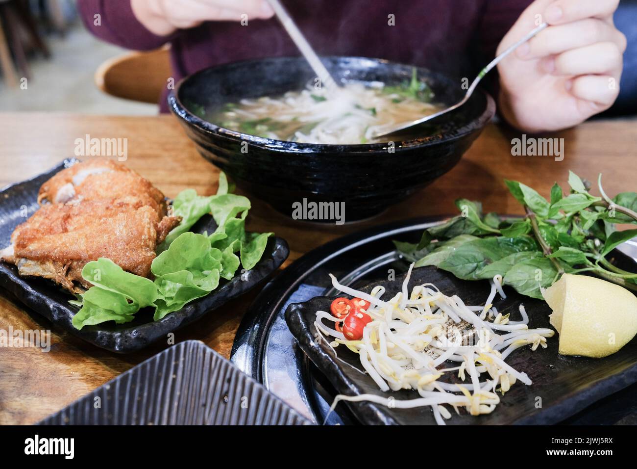 L'uomo mangia una ciotola di Phở Bò (pho di manzo) e Gà da Dòn (pollo a pelle croccante) a Me Pho, un ristorante vietnamita a Bankstown - Sydney, Australia Foto Stock