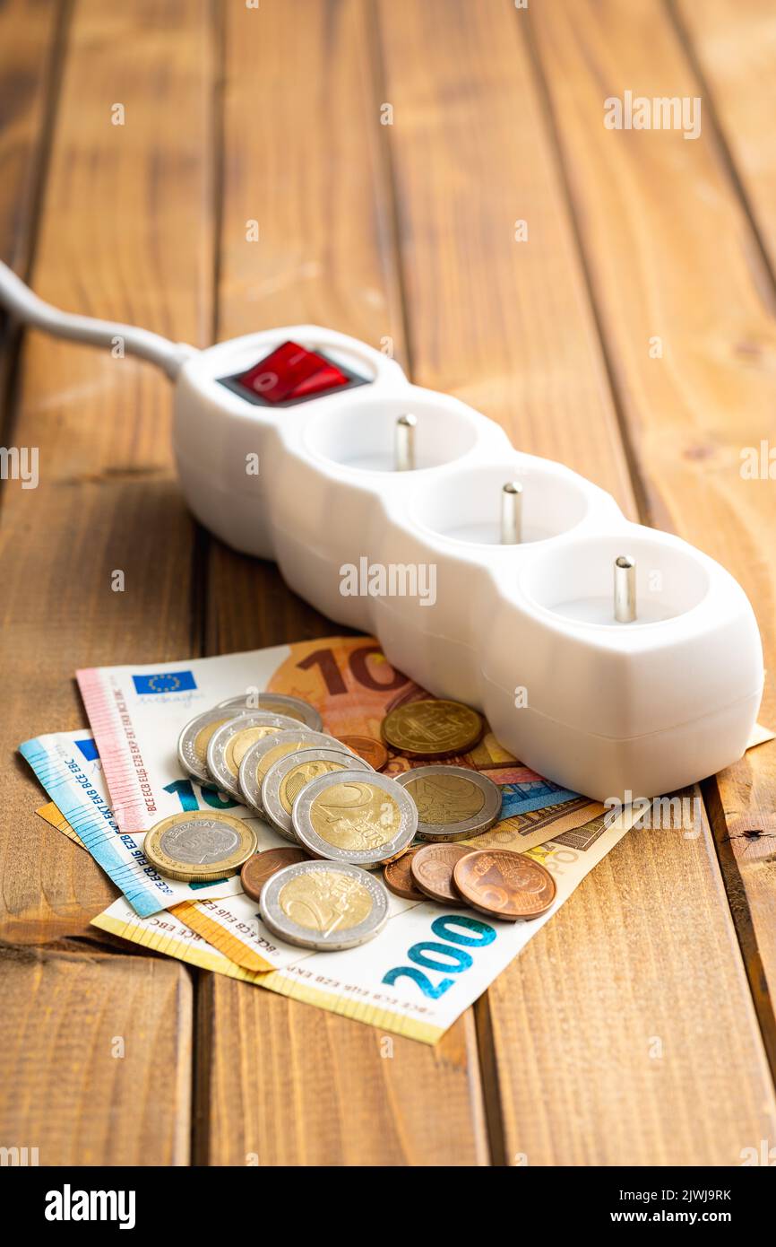 Presa elettrica e denaro in euro sul tavolo di legno. Concetto di aumento dei prezzi elettrici. Foto Stock