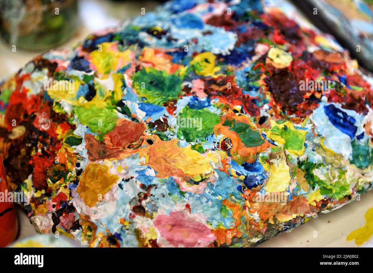 Dall'alto tavolozza ruvida con macchie di vernice multicolore asciutta poste sul tavolo in studio Foto Stock