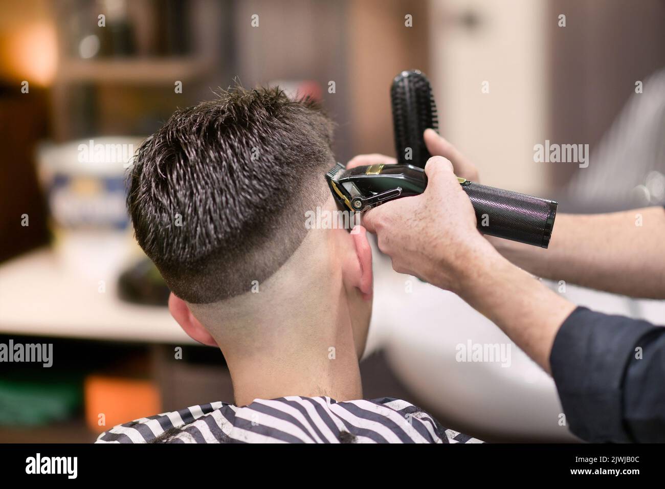 Barbiere maschio irriconoscibile che usa rasoio elettrico per radere i capelli scuri dell'uomo durante il lavoro in barbiere Foto Stock