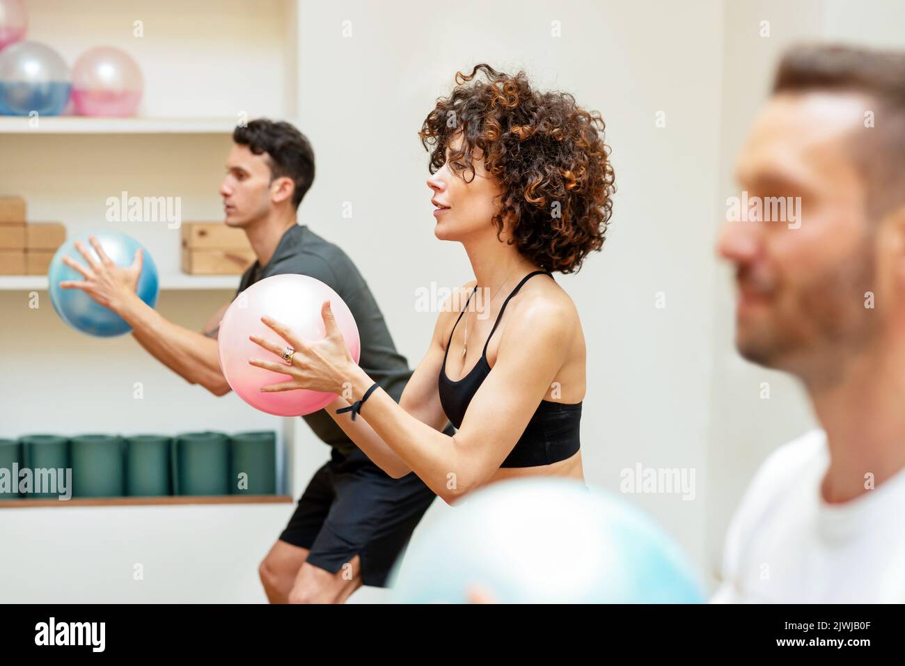 Allenati con i capelli ricci facendo esercizio con il fluiball tra gli sportivi durante l'allenamento di fitness funzionale in palestra Foto Stock