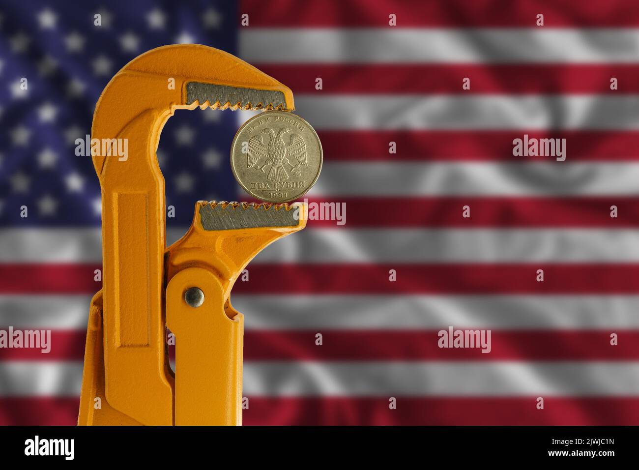 Moneta russa a due rubli tenuta in una chiave per idraulico arancione sullo sfondo della bandiera degli Stati Uniti. Lato opposto della moneta. Foto Stock