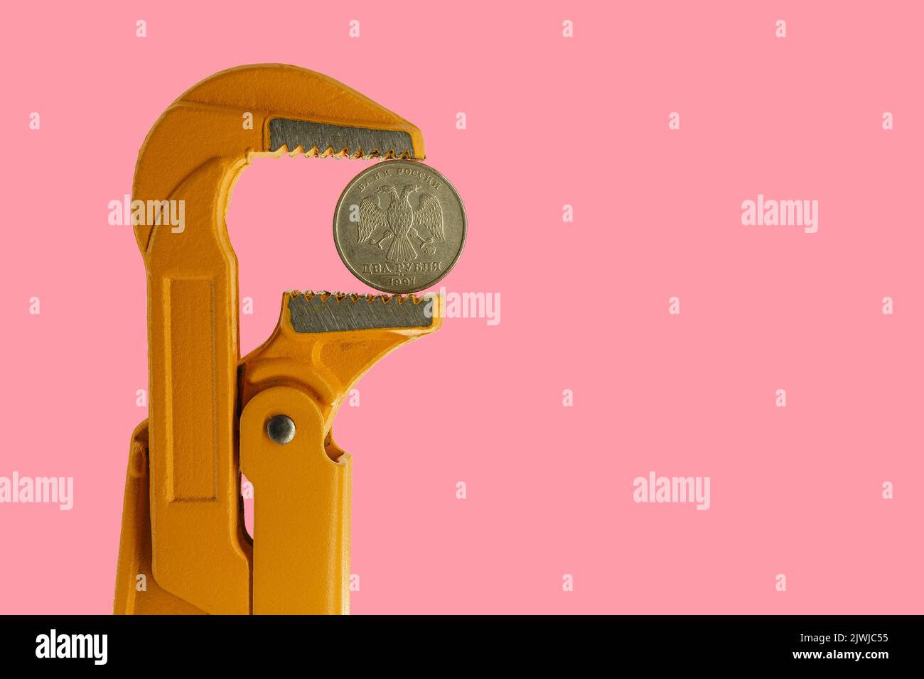 Moneta russa a due rubli tenuta in una chiave per idraulico arancione su sfondo rosa. Lato opposto della moneta. Foto Stock