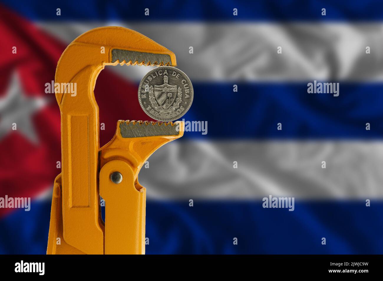 Tre pesos cubani tenuti in una chiave per idraulico arancione sullo sfondo della bandiera cubana. Foto Stock