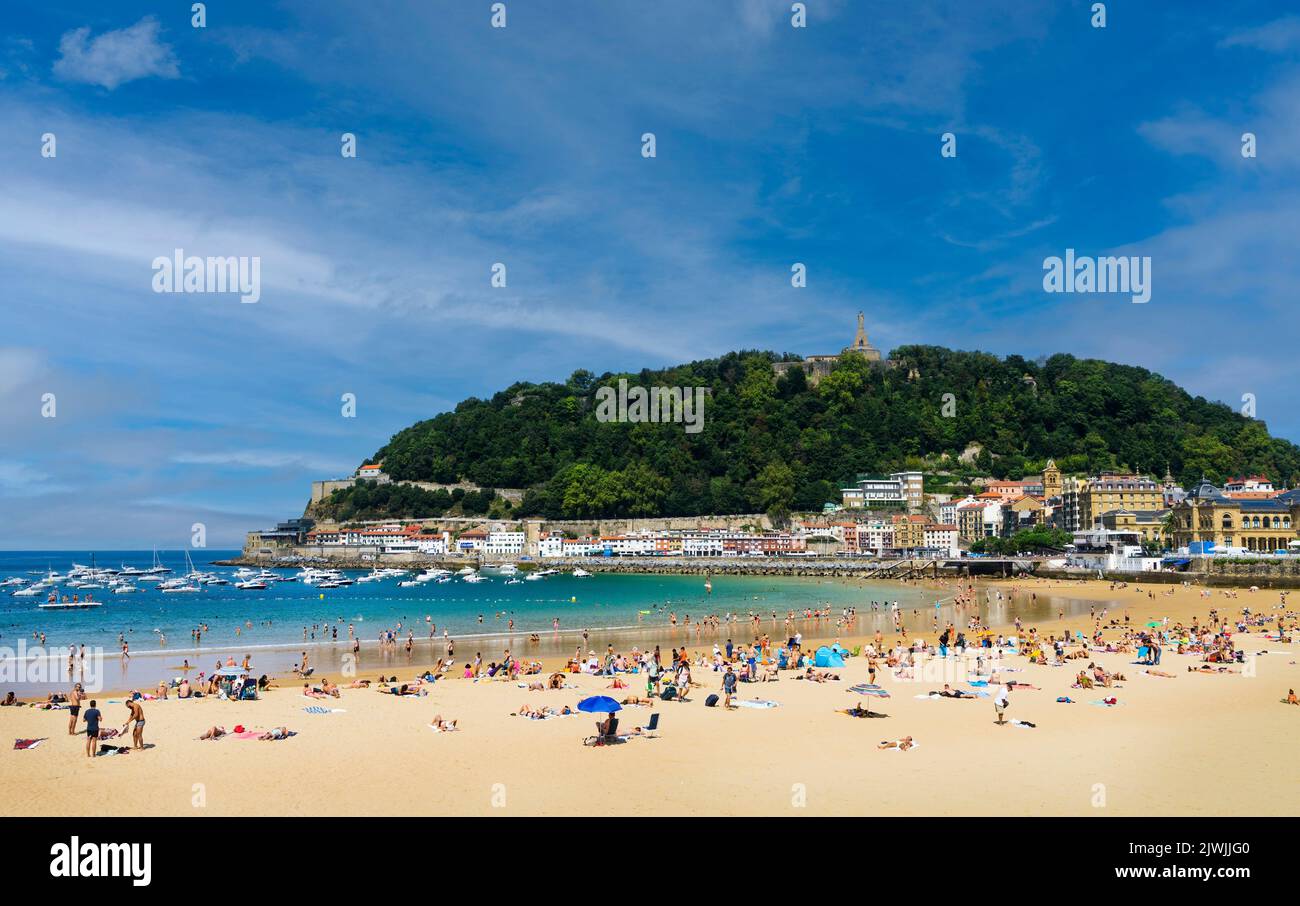 Paesaggio della spiaggia di la Concha nella città di San Sebastian, nei Paesi Baschi spagnoli, in una giornata di sole con la gente che si gode la spiaggia e il Monte Urgu Foto Stock