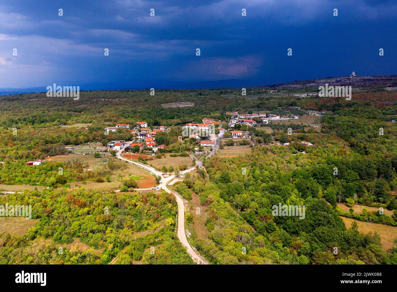 Vista aerea di un bellissimo piccolo villaggio, tradizionale villaggio carsico nella zona di Komen, in un giorno d'estate soleggiato, poco prima della tempesta, in Slovenia Foto Stock