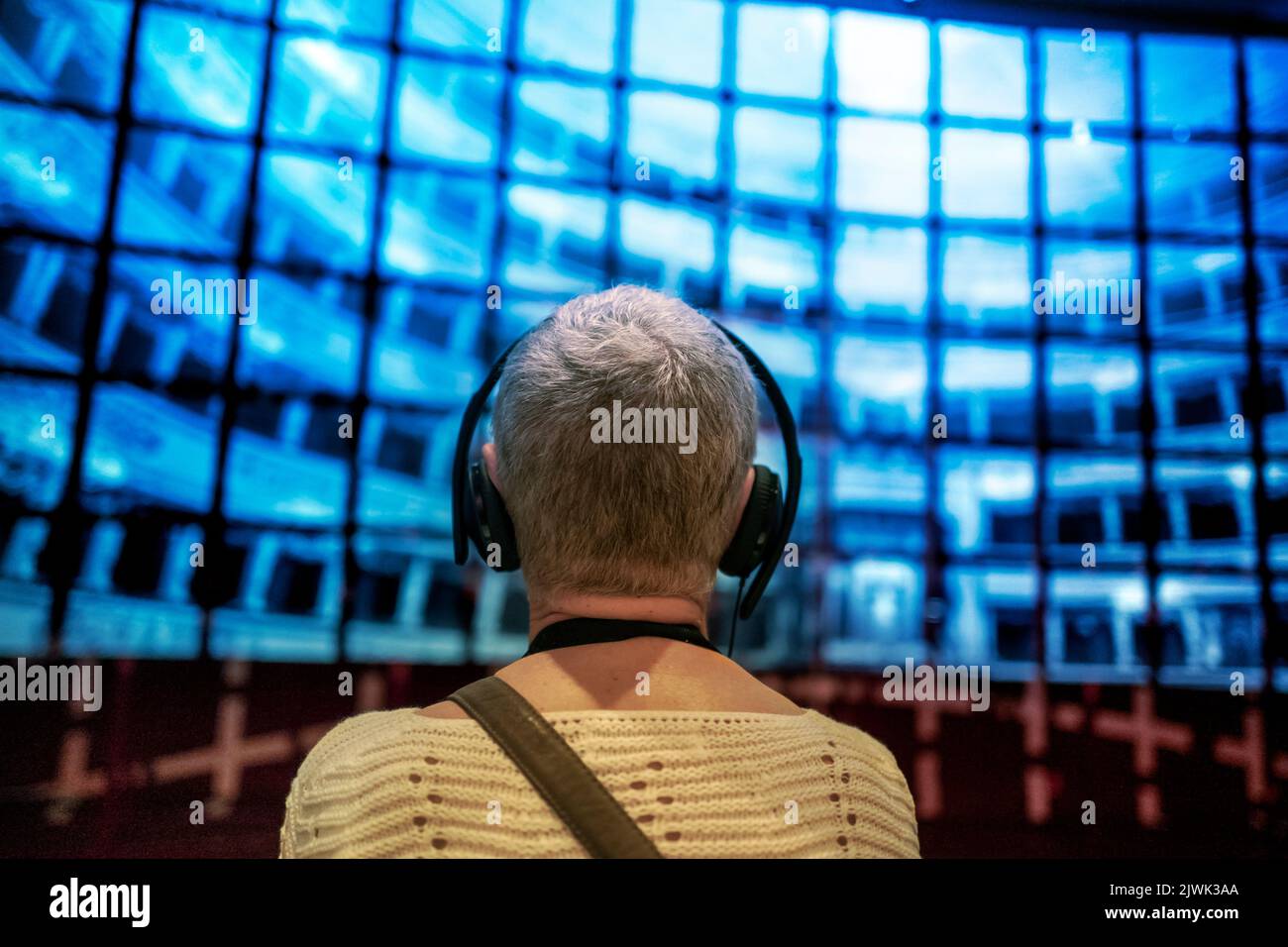Donna anziana con cuffie di fronte alla proiezione di schermi multimediali. Messa a fuoco superficiale sullo sfondo Foto Stock