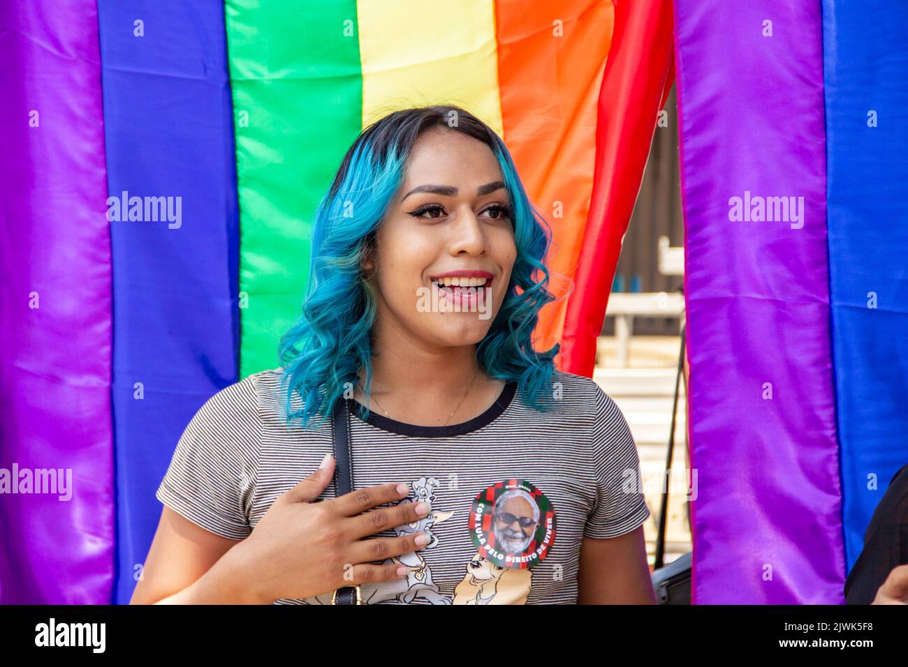 Goiânia, Goias, Brasile – 04 settembre 2022: Una ragazza sorridente, i suoi capelli tinti di blu con bandiere arcobaleno sullo sfondo. Foto scattata durante la Parata. Foto Stock