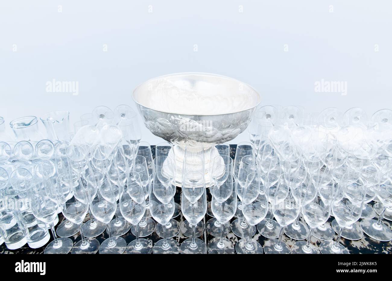 Vetreria vuota sul tavolo, bicchieri allineati pronti per feste, eventi, riunioni, vista frontale sfondo bianco Foto Stock