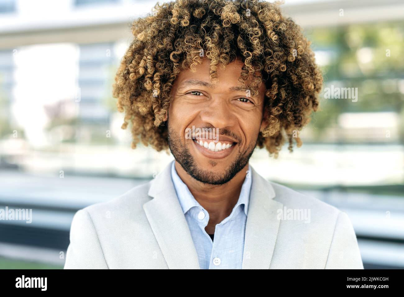 Foto ravvicinata di un uomo da corsa misto, brasiliano o imprenditore latino, dirigente aziendale, elegante e sicuro, con capelli ricci, che guarda la fotocamera, sorridendo amichevole Foto Stock