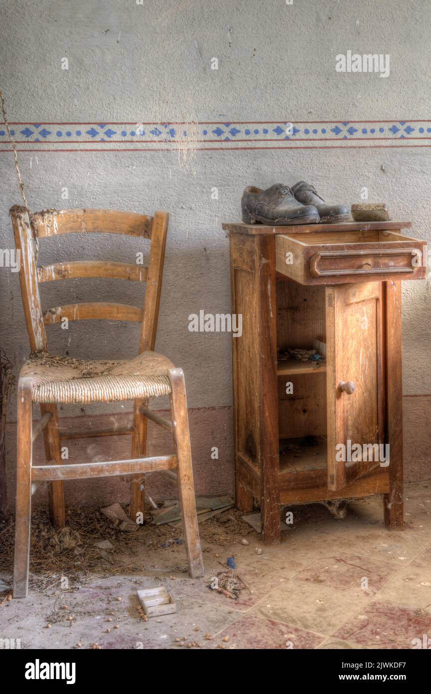 Italia, 09-10-2023. Vecchia sedia e comodino con un paio di scarpe decadenti. In una vecchia casa di campagna abbandonata nel nord Italia Foto Stock