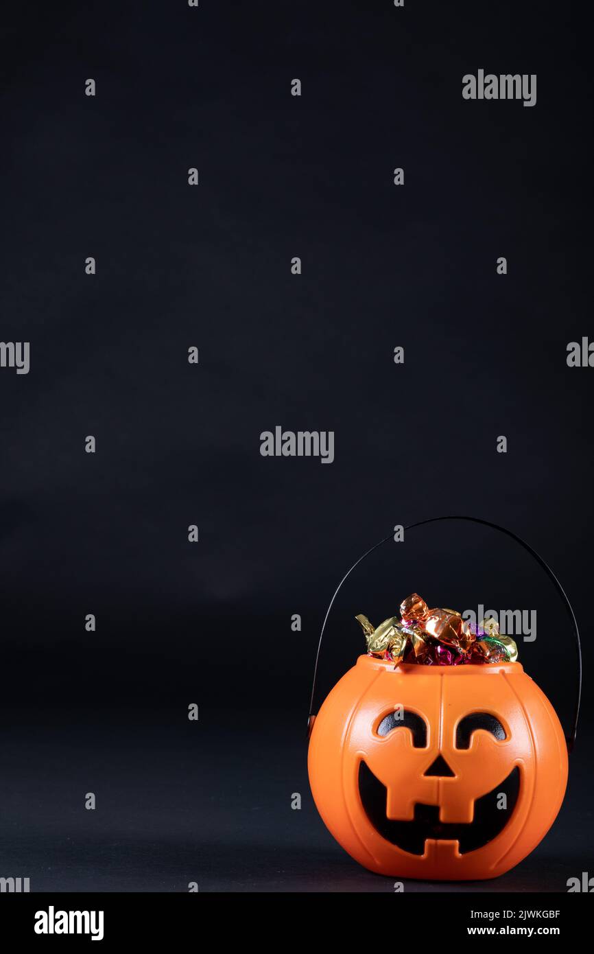 Secchio a forma di zucca di Halloween pieno di caramelle su sfondo nero Foto Stock