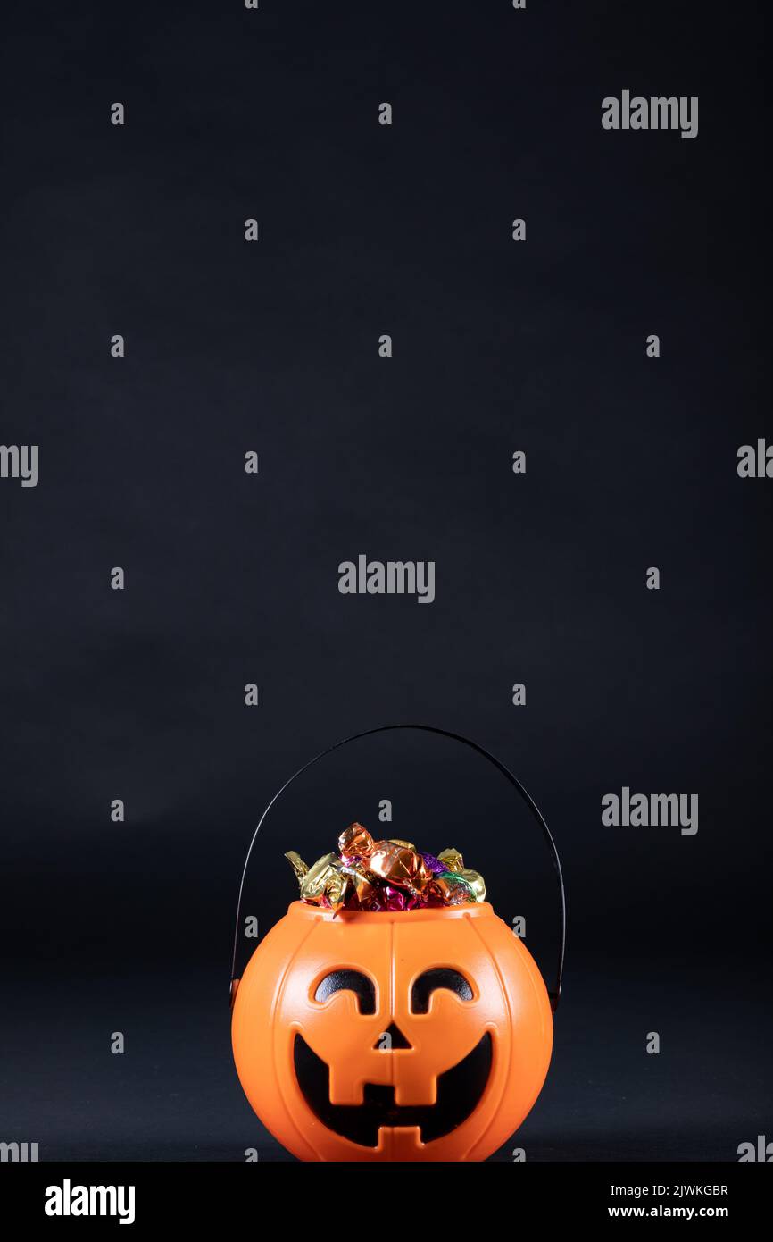 Secchio a forma di zucca di Halloween pieno di caramelle su sfondo nero Foto Stock