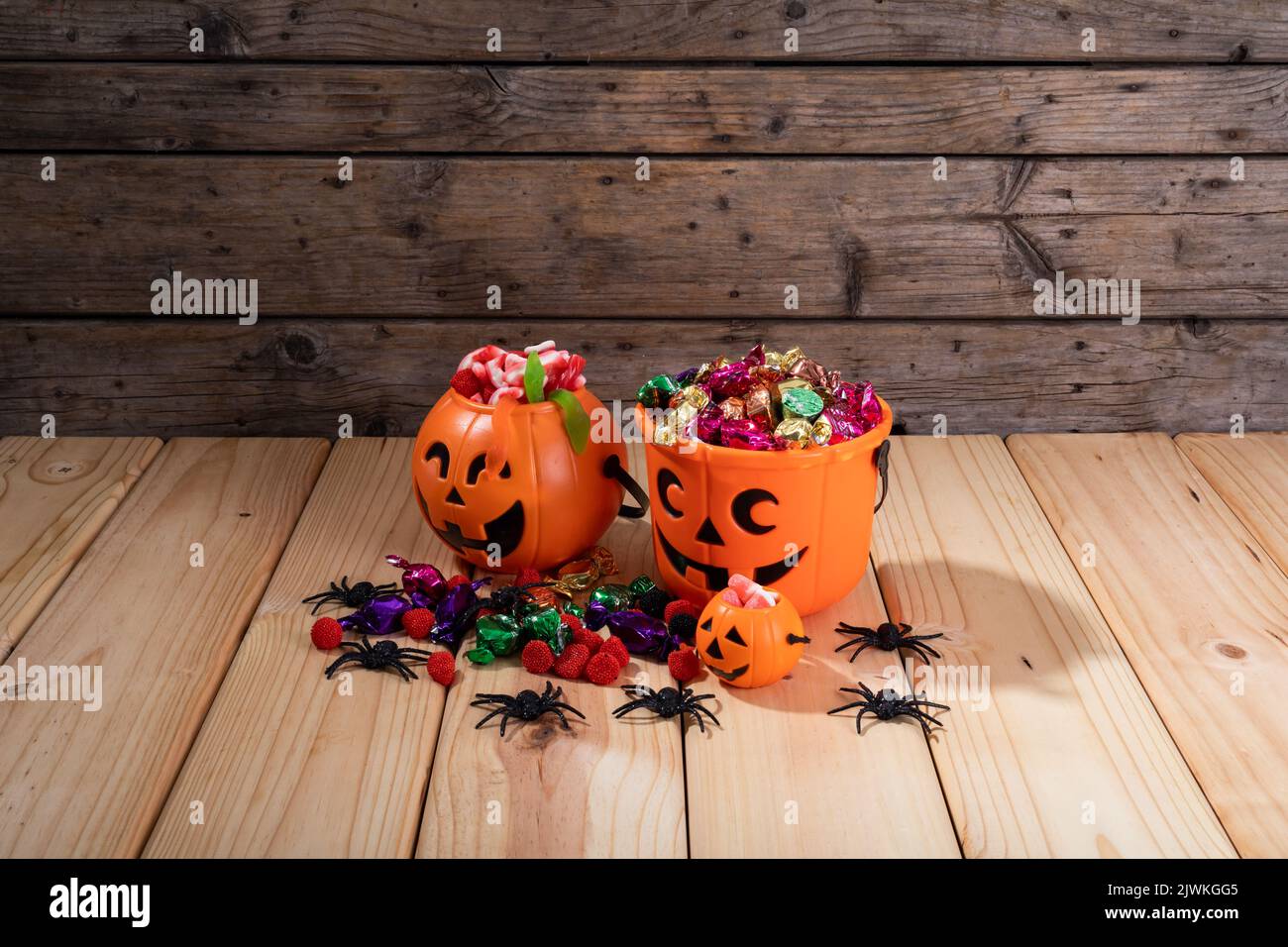 Secchio a forma di zucca pieno di caramelle di Halloween e giocattoli su superficie di legno Foto Stock
