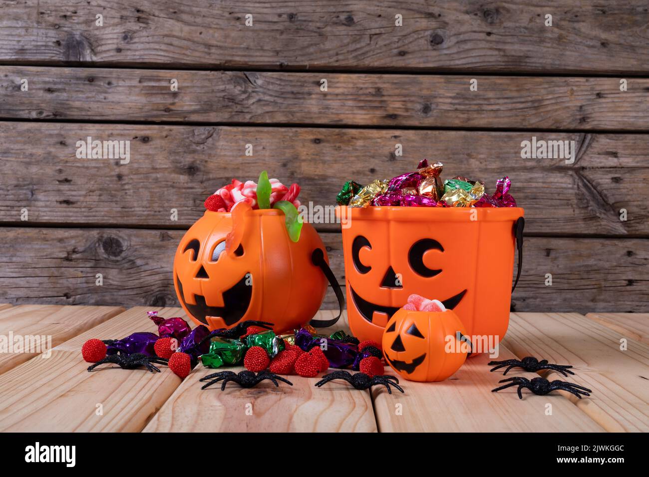 Secchio a forma di zucca pieno di caramelle di Halloween e giocattoli su superficie di legno Foto Stock