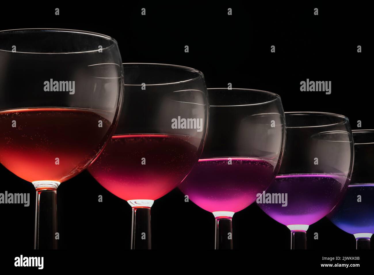 Bicchieri multicolori con diversi vini coda di cocco - viola blu rosso su uno sfondo nero bicchieri in fila. Foto Stock