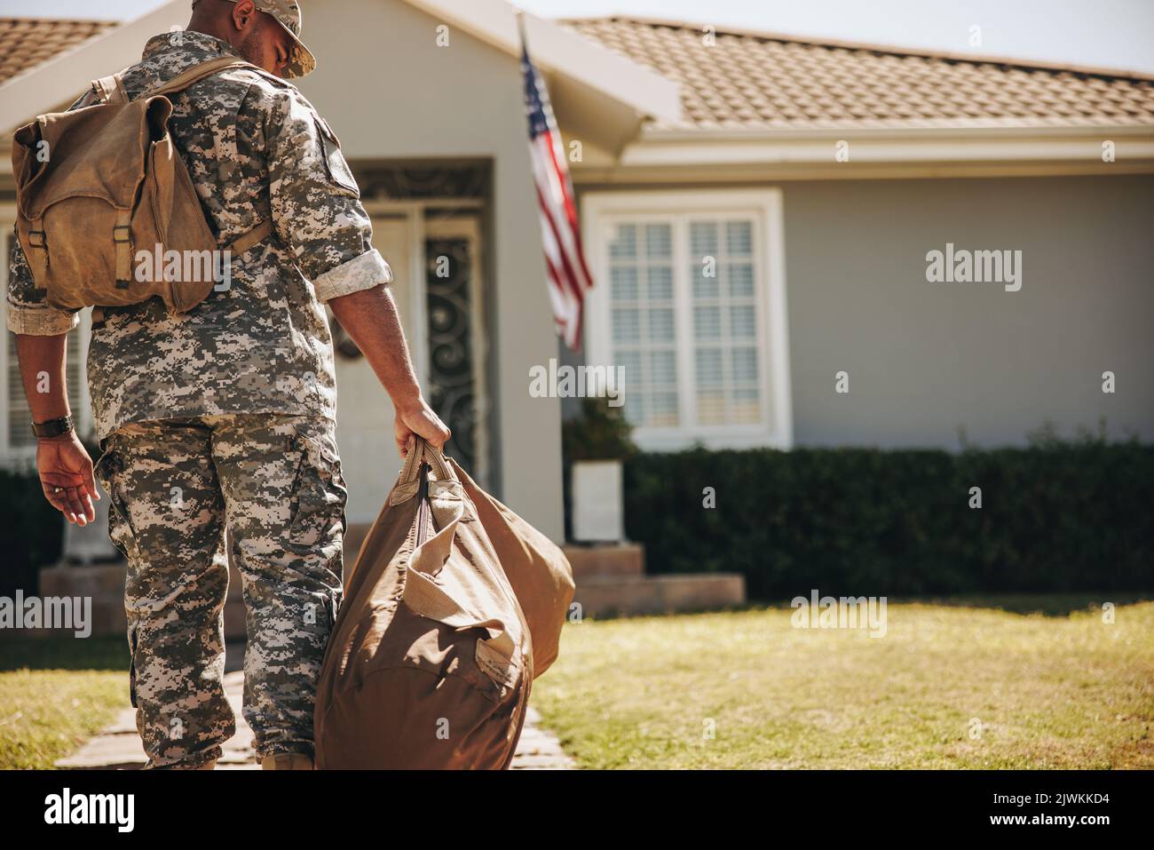 Vista posteriore di un giovane soldato patriottico che porta i bagagli fuori casa. Serviceman americano tornando a casa dopo aver prestato servizio militare. Foto Stock