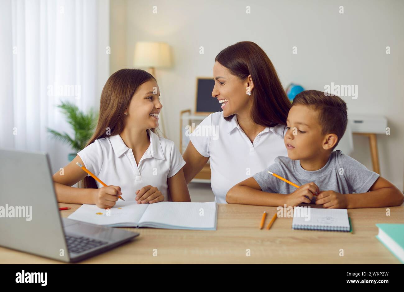 Madre felice e bambini piccoli che si divertono mentre fanno i compiti a scuola insieme Foto Stock