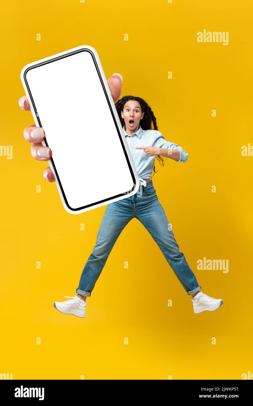 Scioccata Signora araba che mostra lo schermo del telefono su sfondo giallo, verticale Foto Stock