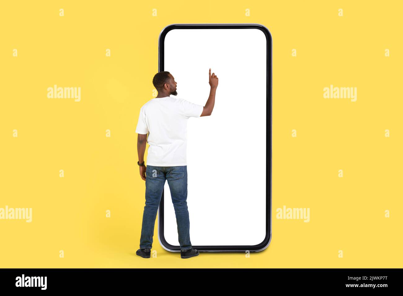 Uomo nero che usa lo schermo enorme del telefono, sfondo giallo, vista posteriore Foto Stock