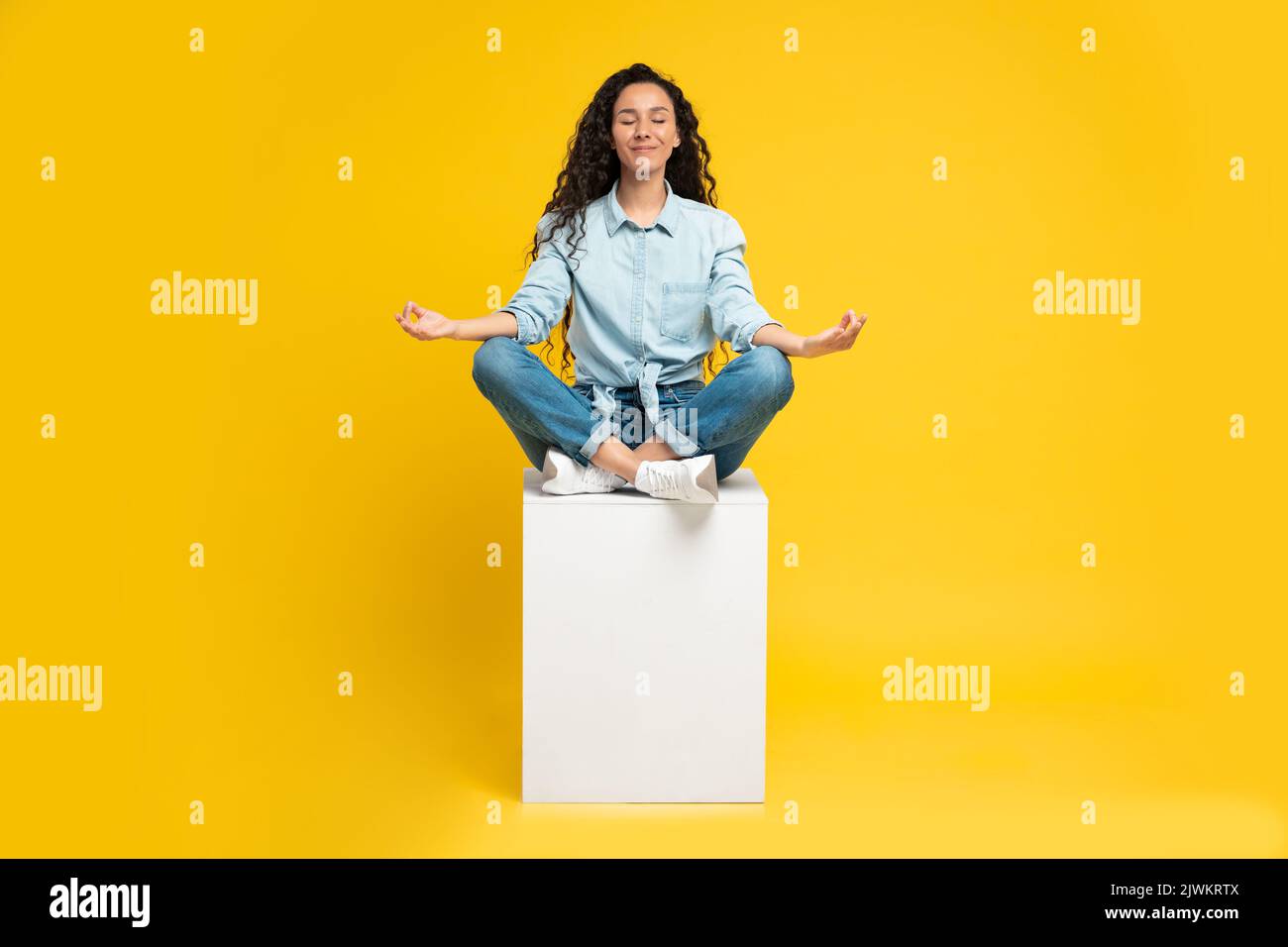 Donna mediorientale meditando con gli occhi chiusi su sfondo giallo Foto Stock