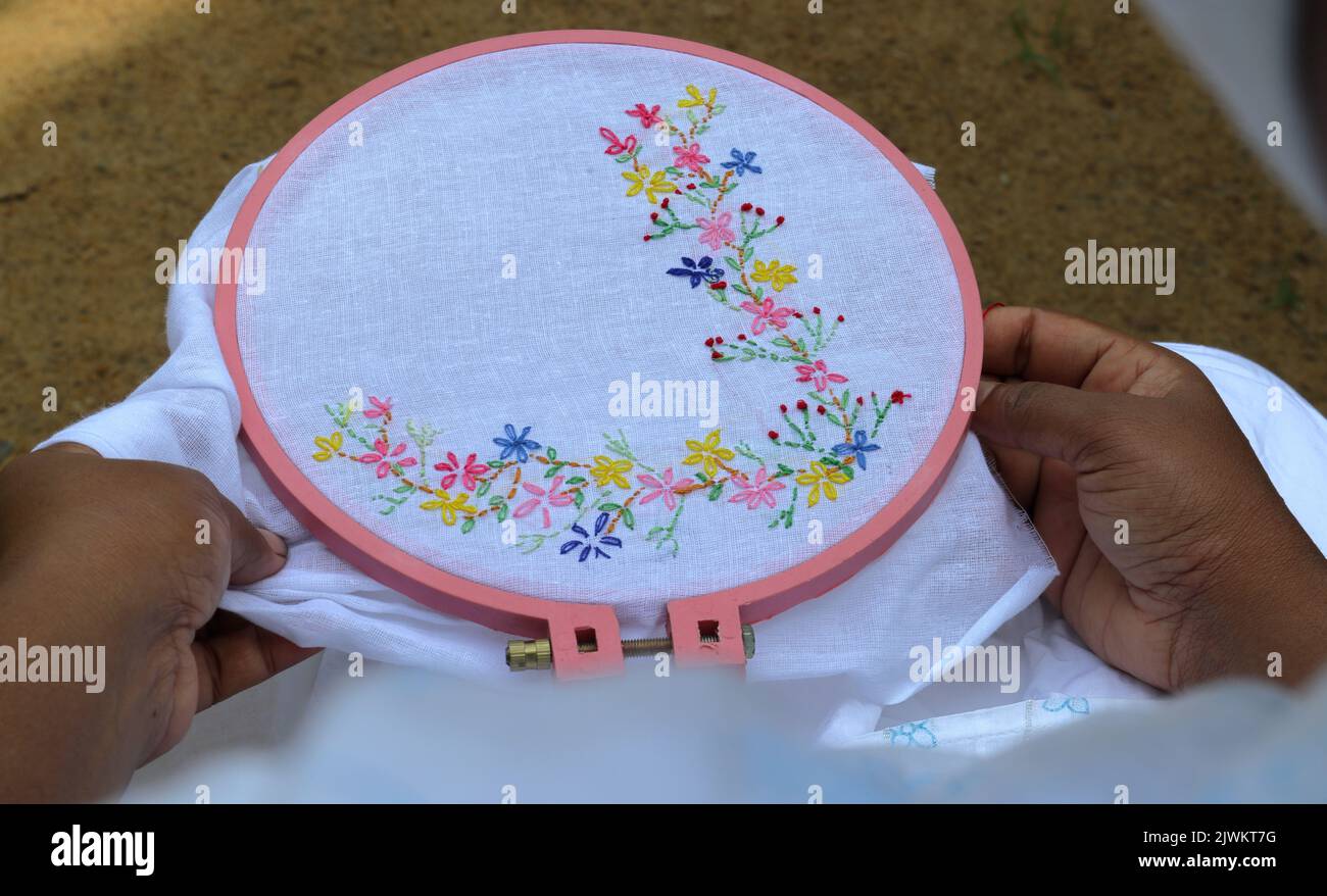 Sopra la vista della spalla di una donna asiatica che crea un ricamo a mano Lazy Daisy Stitch su un cloth.on questo bianco tessuto piccoli fiori con foglie sono craf Foto Stock