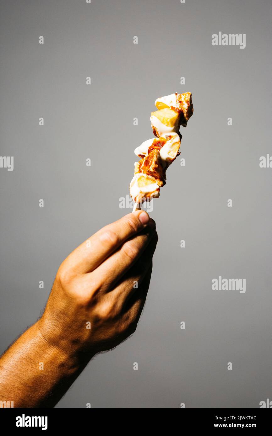 Mano umana che tiene una broccia di patate fritte con maionese e salsa di pomodoro spato su uno sfondo grigio Foto Stock