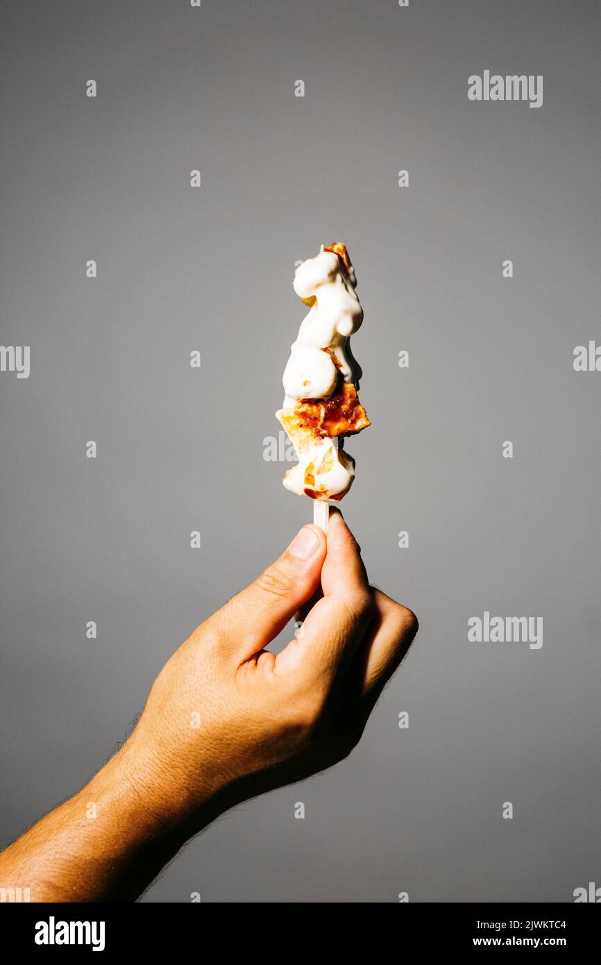 Mano umana che tiene una broccia di patate fritte con maionese e salsa di pomodoro spato su uno sfondo grigio Foto Stock