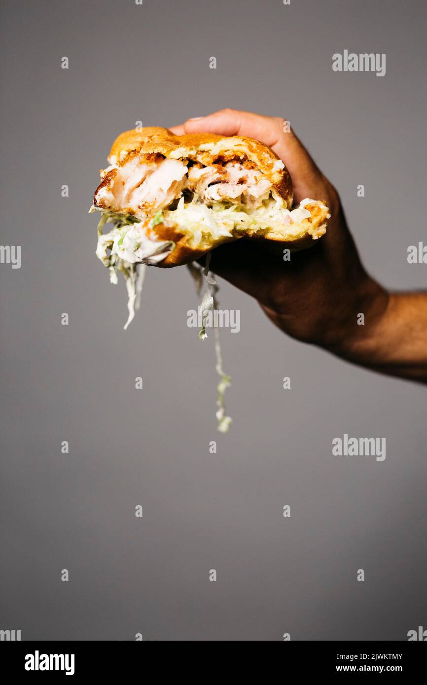 Mano umana che tiene un hamburger di maiale morso con lattuga su uno sfondo grigio Foto Stock