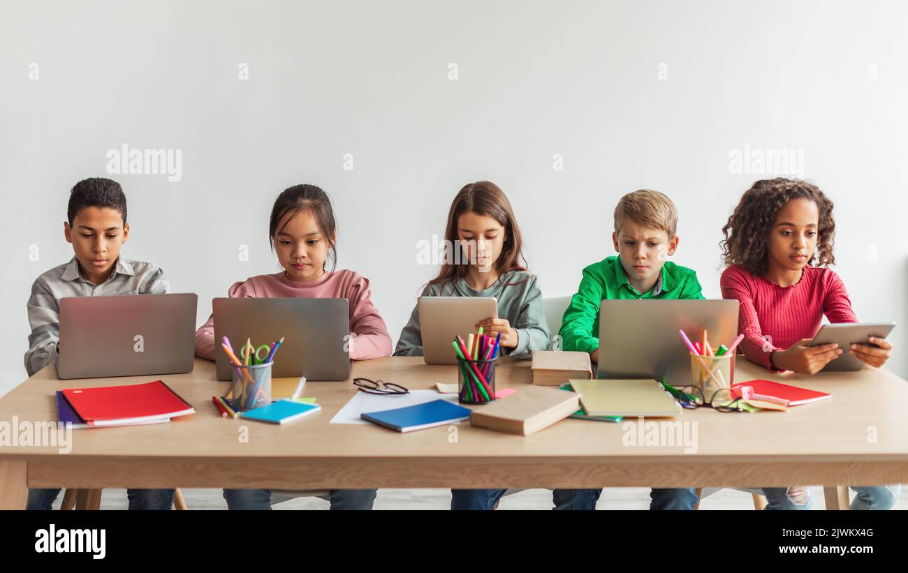 Cinque ragazzi di scuole multietniche che utilizzano i notebook in aula, Panorama Foto Stock