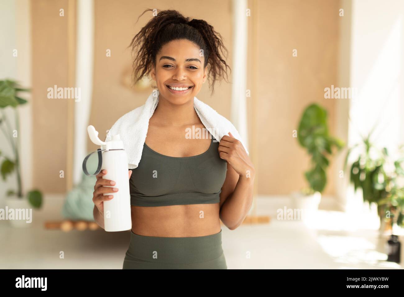 Nutrizione per lo sport e l'esercizio fisico. Donna afro-americana felice con asciugamano bianco sul collo che tiene shaker con proteine Foto Stock