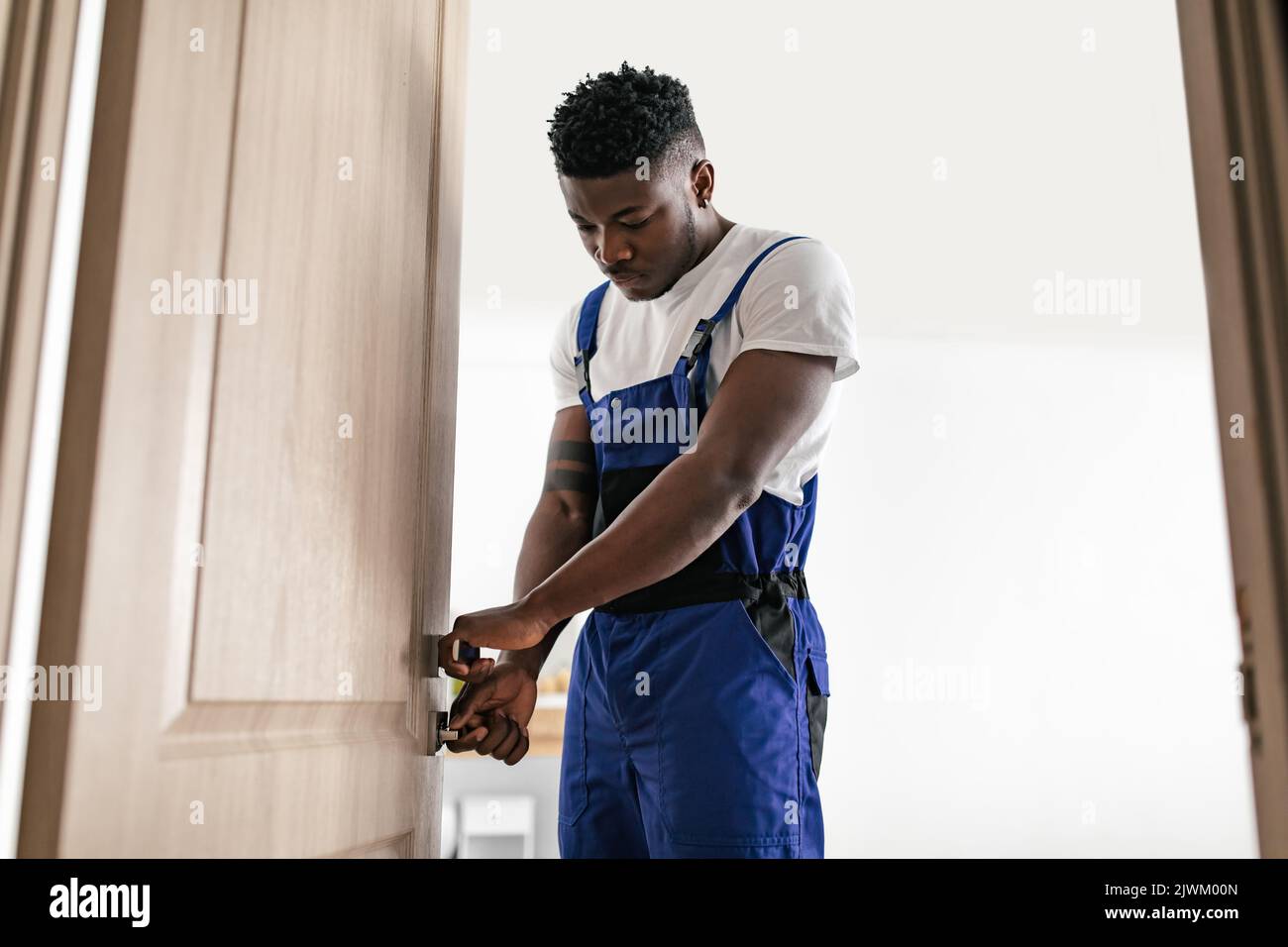 African American riparatore che fissa la porta in piedi indoor, che indossa tuta Foto Stock