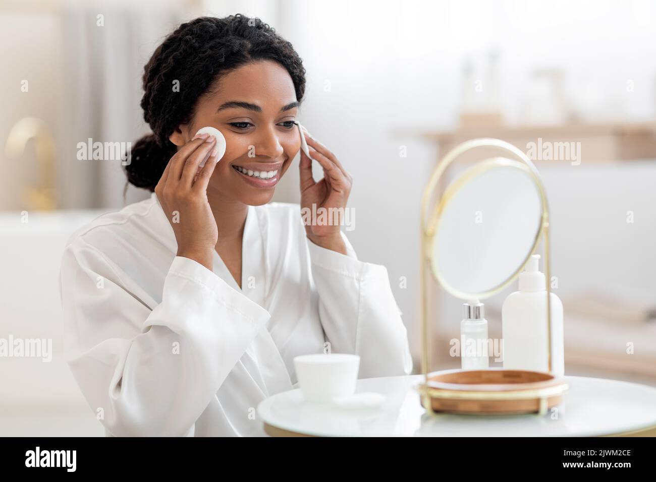 Bella donna nera che guarda specchio e pelle detergente con tamponi in cotone Foto Stock
