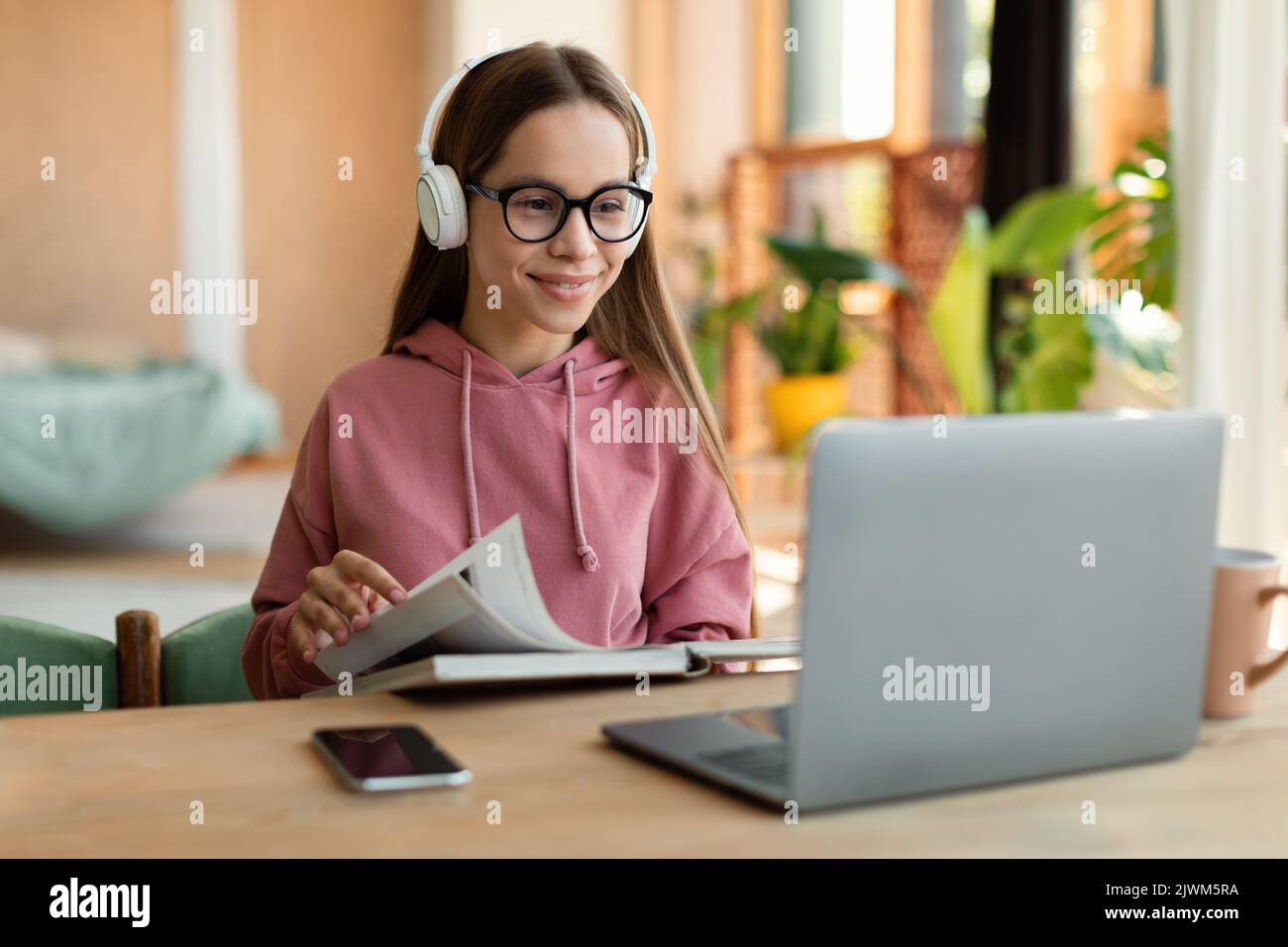 E-learning, concetto di formazione basato sul web. Ragazza felice teen che studia online da casa, leggendo il libro e guardando il laptop Foto Stock