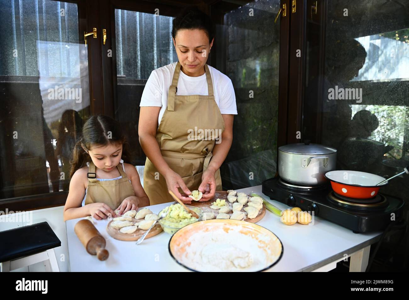 Amando la giovane madre e la sua adorabile bambina nei grembiuli dello chef, divertiti a fare gli gnocchi fatti in casa insieme, a stendere l'impasto e a farcire schiacciati Foto Stock