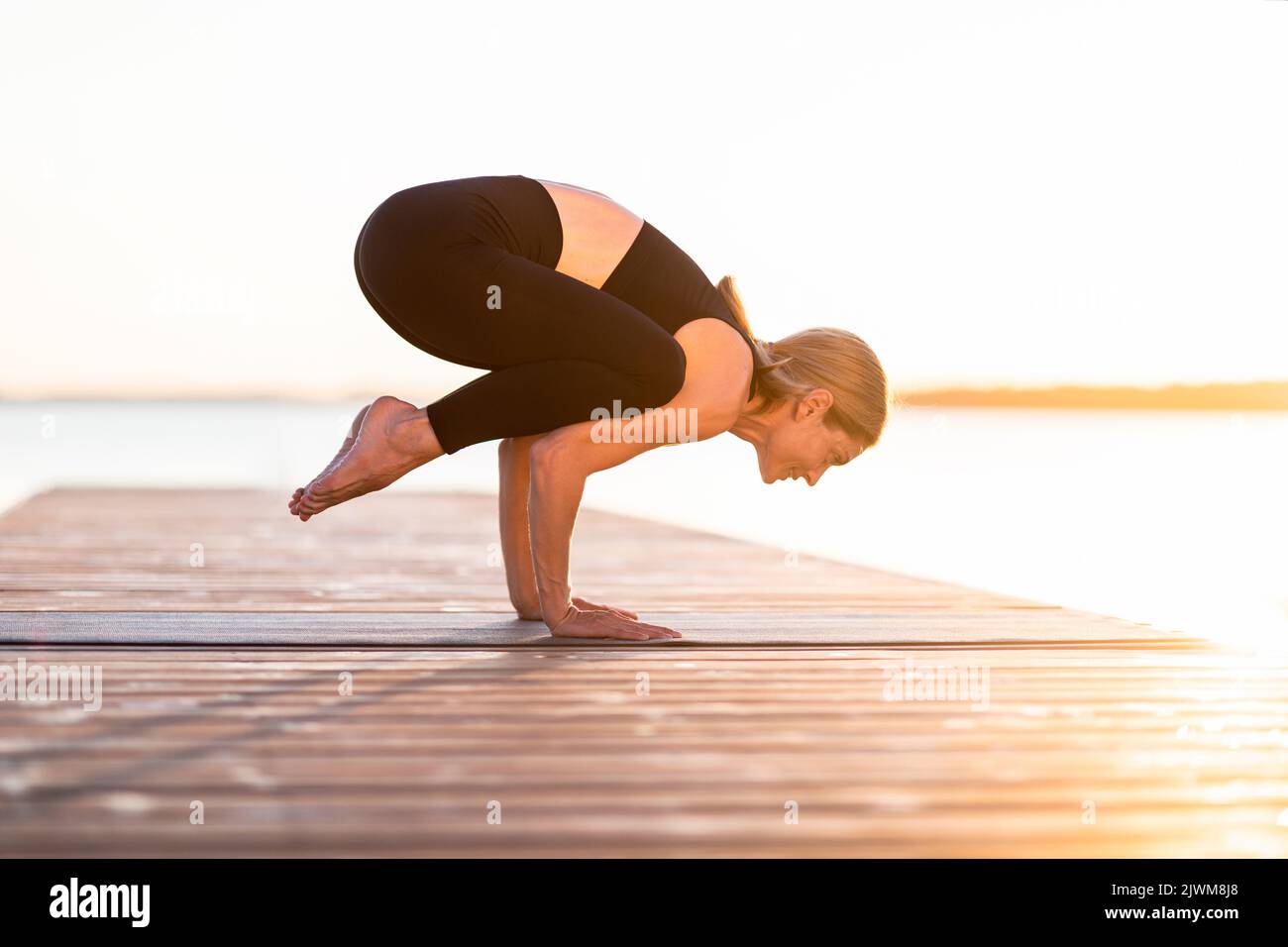 Donna sportiva di mezza età in piedi in posizione Corvo mentre si pratica lo yoga all'aperto Foto Stock